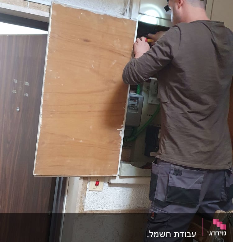 חשמלאי עובד על לוח חשמל עם מברג ביד